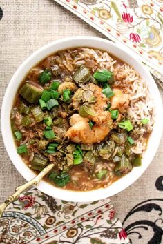 a white bowl filled with shrimp and rice on top of a floral table cloth next to a spoon