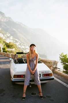 a woman sitting on the hood of a white sports car in front of a mountain