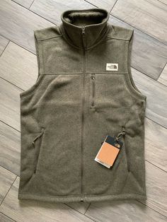 NORTH FACE MENS GORDON LYONS VEST, TAUPE GREEN HEATHER, NWT $89, S.  This North Face mens Gordon Lyons Vest in the color Taupe Green Heather is brand new with the tag attached.  The product description is: FEATURES  Standard fit Recycled Gordon Lyons sweater-knit fleece with a brushed backer Exposed, reverse-coil center front zip Secure-zip chest pocket and hand pockets This men's Gordon Lyons Vest is a men's size small.  The measurements laying flat on the floor are:  chest - 20 inches, shoulde Casual Green Vest For Fall, Green Casual Vest For Fall, Sleeveless Vest For Fall Hiking, Sleeveless Green Outerwear For Fall, Khaki Hiking Vest For Fall, Khaki Vest For Hiking In Fall, Winter Khaki Tops For Outdoor Activities, Green Winter Vest For Outdoor Activities, Khaki Tops For Outdoor Winter Activities