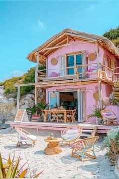 a pink house on the beach with chairs and tables in front of it that is built into the sand