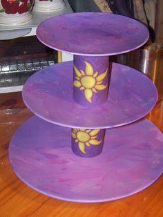 three tiered cake stand with purple frosting and yellow designs on the top, sitting on a wooden table