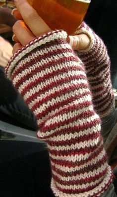 a woman holding up a cup of tea in her right hand while wearing knitted mitts