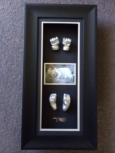 a baby's hand and foot casts in a shadow box with black mating