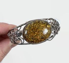 "Stunner! This is a vintage sterling silver bracelet set with a large piece of polished Tony amber. The amber is accented with leaves and flowing sterling accents that curl here and there. This is a hinged cuff or bangle bracelet. It closed with a side slide claps and has a safety chain. So pretty and is inspired by the Art Nouveau style. Condition: Very good vintage condition, vintage patina Measurements: 6 3/4\" inside Width: 0.96\" or 24.45 mm wide Weight: 26.2 grams Markings: Unmarked, teste Vintage Amber Bangle Bracelet, Handmade Vintage Sterling Silver Bracelets, Victorian Bracelets With Polished Finish As Gift, Antique Silver Cabochon Bracelets, Victorian Bracelets With Polished Finish, Victorian Bracelet With Polished Finish As Gift, Vintage Amber Jewelry With Engraved Details, Handmade Victorian Sterling Silver Bracelets, Vintage Handmade Sterling Silver Bracelet In Antique Silver