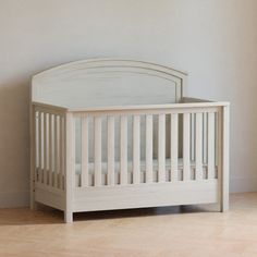 a white crib sitting on top of a hard wood floor next to a wall