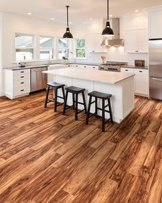 a large kitchen with white cabinets and wooden flooring, two stools at the island