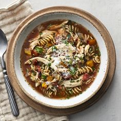 a white bowl filled with pasta and vegetables on top of a table next to a spoon