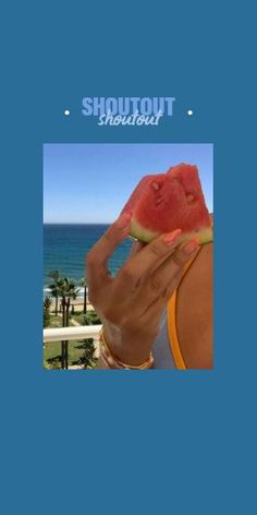 a woman holding up a piece of watermelon in front of the ocean