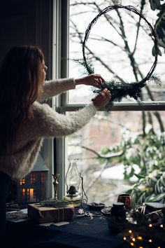 a woman hanging a wreath on the window sill