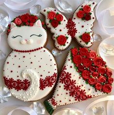 three decorated cookies with red roses and white frosting on them, one is shaped like a cat