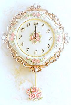 a white clock with pink flowers on the front and sides, hanging from a wall