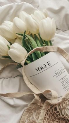 a bouquet of white tulips sitting on top of a bed next to a book