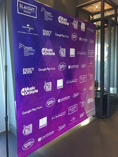 a large purple banner in front of a glass wall with various logos on it and people walking by