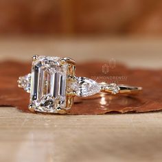 an emerald and diamond ring sitting on top of a wooden table next to a leaf