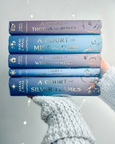 a person holding four books in their hands with snow flakes behind them and the text, a court of mist and fury