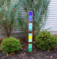 a tall multicolored wooden pole in front of some bushes and trees on the side of a house