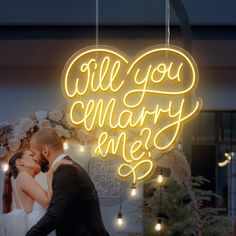 a bride and groom kissing under a neon sign that says will you marry me?