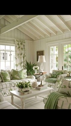 a living room filled with lots of white furniture and green pillows on the couches