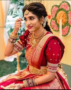 a woman in a red and gold bridal outfit sitting on the ground with her hand up to her face