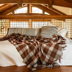 an unmade bed with plaid blankets and pillows on it in a room that has wooden beams