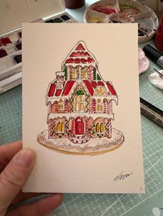 a hand holding up a card with a drawing of a gingerbread house on it