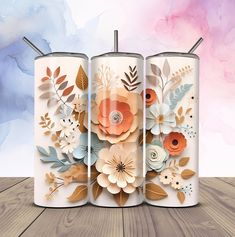 three candles with floral designs on them sitting on a wooden table in front of a watercolor background