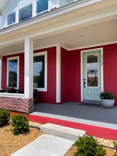 a red house with white trim and two large windows on the front porch, along with potted plants