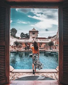 a woman standing in front of an open window looking out at a pool and buildings