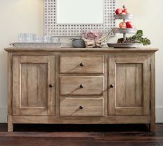 a wooden buffet table topped with lots of fruit and veggies next to a mirror