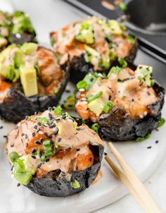 some stuffed mushrooms are topped with sauce and vegetables, along with chopsticks on the side