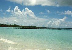 the water is very blue and clear with some clouds in the sky above it on a sunny day