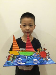 a young boy holding up a paper boat with sailboats on the front and sides