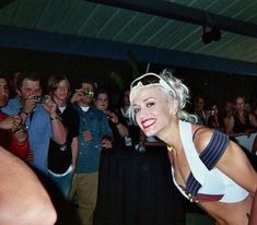 a woman with white hair and sunglasses standing in front of a group of people at a party