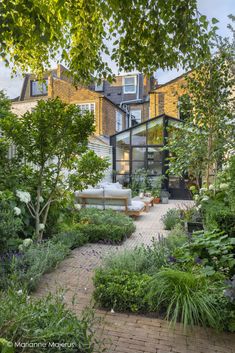 an outdoor garden with lots of plants and trees in front of the house, surrounded by greenery