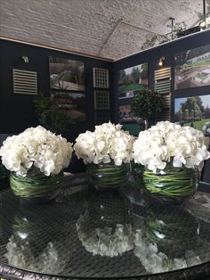 three vases filled with white flowers on top of a glass table