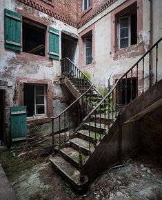 an old run down building with green shutters on the windows and stairs leading up to it