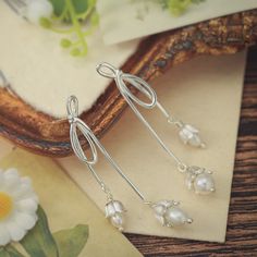 Elevate your elegance with our Silver Lily Of The Valley Bow Earrings. Crafted in sterling silver, these delicate earrings showcase the iconic Lily of the Valley motif in a charming bow design. A touch of femininity and nature-inspired grace, these earrings are perfect for adding a subtle yet timeless accent to your look.  🎀 DETAILS Materials:  Sterling  Silver, Pearl Size: 2.09"* 0.31 "(5.3cm*0.8cm) Weight: 7.4g/pr Sterling Silver Drop Clip-on Earrings For Gift, Silver Sterling Pearl Drop Flower Earrings, Silver Sterling Flower Earrings With Pearl Drop, Silver Flower Earrings With Pearl Drop, Sterling Silver Drop Earrings For Anniversary, Silver Single Elegant Flower Earring, Adjustable Delicate Silver Earrings, Sterling Silver Dangle Pearl Earrings For Pierced Ears, Dainty Silver Pearl Earrings For Gift