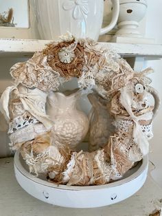 a white vase sitting on top of a table next to a wreath with laces