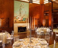 a room filled with tables and chairs covered in white tablecloths next to a fire place