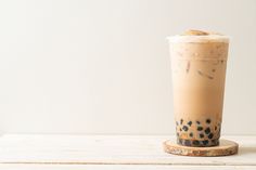 there is a drink in the glass on top of a wooden table with a white wall behind it