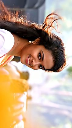 a woman with long hair standing next to a yellow car and smiling at the camera