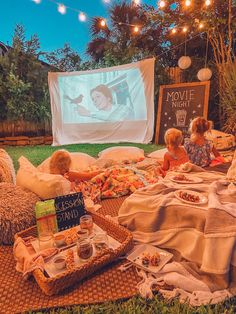 two children are sitting on the grass in front of a movie screen and eating food