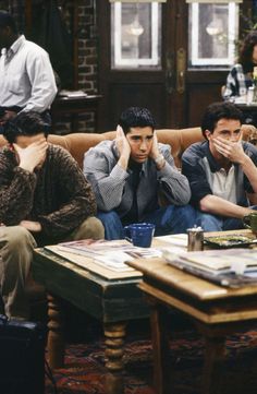 three men sitting on a couch in a living room with one man covering his face