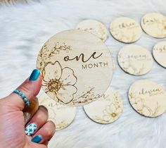 a person holding up a wooden coaster with flowers on it and the words one month printed on it