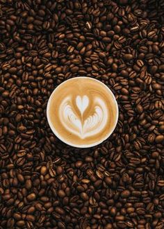 a cappuccino in the shape of a heart on top of coffee beans