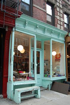 an empty bench in front of a store on a city street with lots of windows