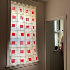 a window with red squares on it and a white curtain in the corner next to an open door