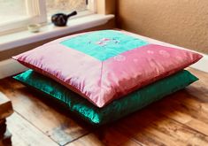 three pillows stacked on top of each other in front of a window with a teal green and pink color scheme