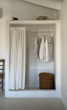 an open closet with white curtains and clothes hanging on the wall, next to a basket