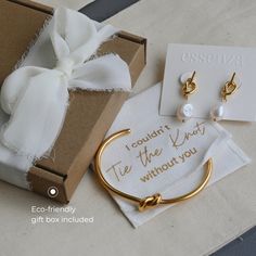 a gift box with some gold jewelry and a white ribbon tied around it, sitting on a table